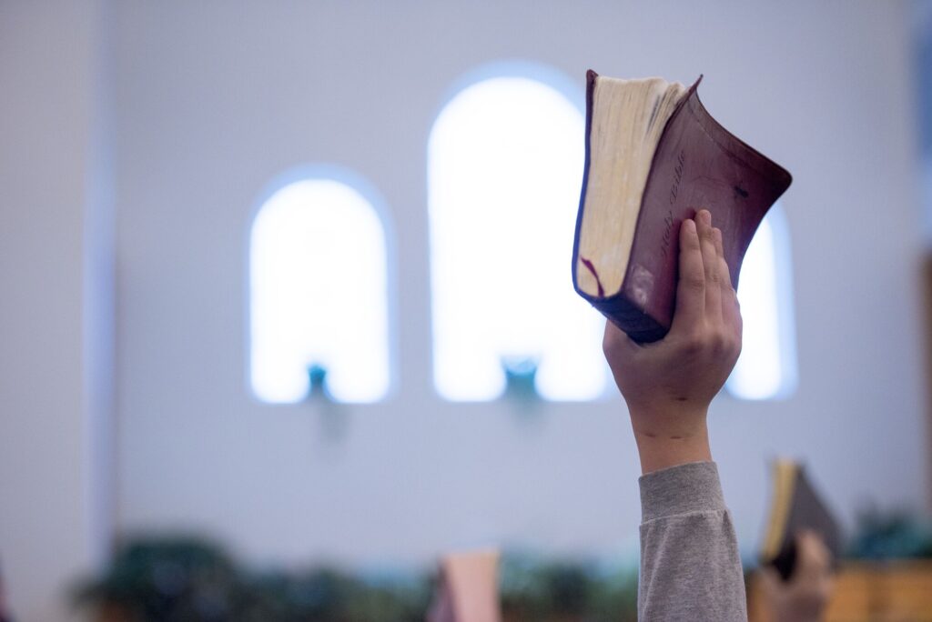 Mão erguendo uma Bíblia dentro de uma igreja iluminada