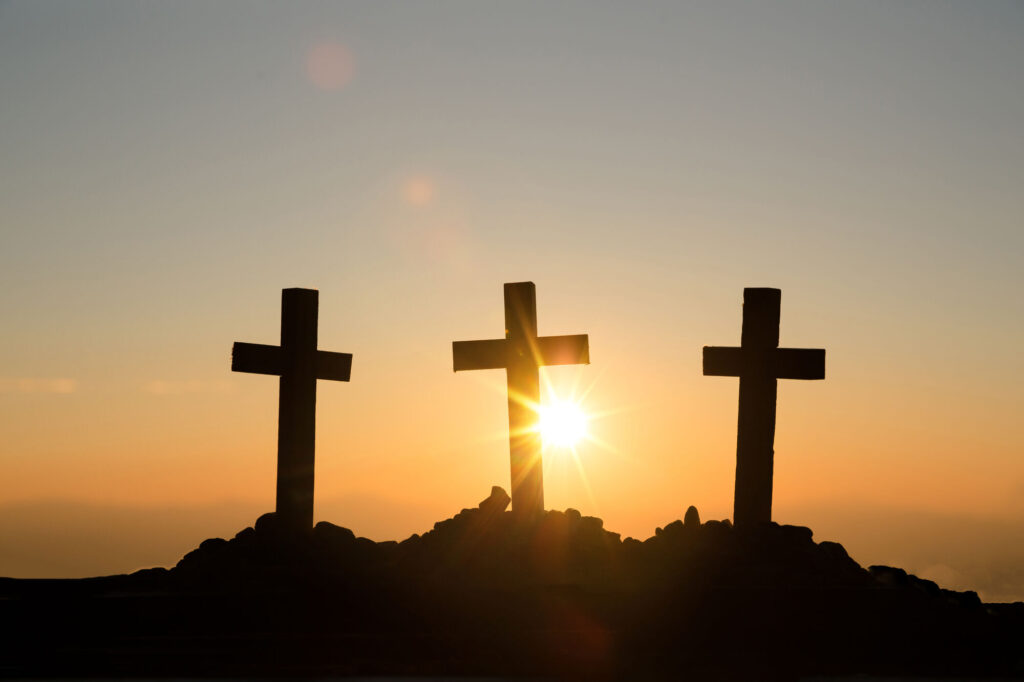 Três cruzes em silhueta no alto de um monte ao pôr do sol